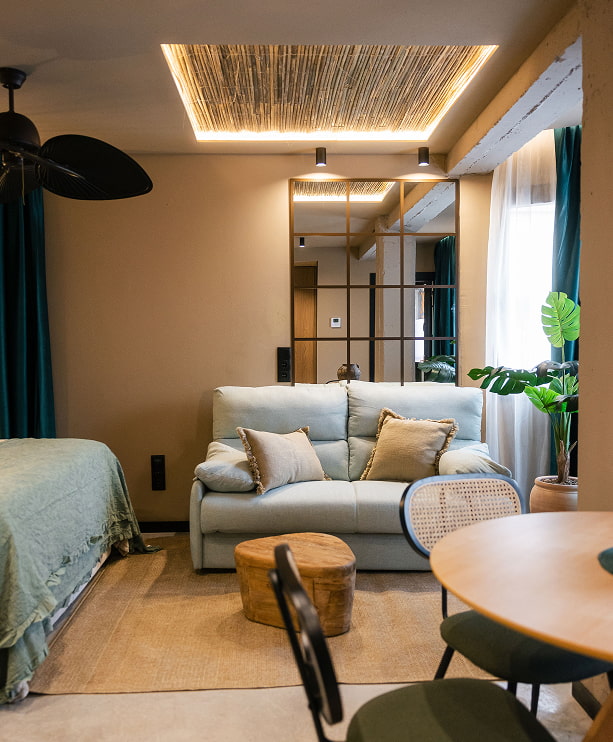 Apartamentos Grupo CCOMMO Estudio con cama, sofá, mesa baja de madera y techo de cañizo iluminado en un apartamento turístico de Murcia